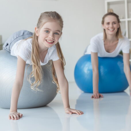 smiling mother and daughter lying on fit balls at home